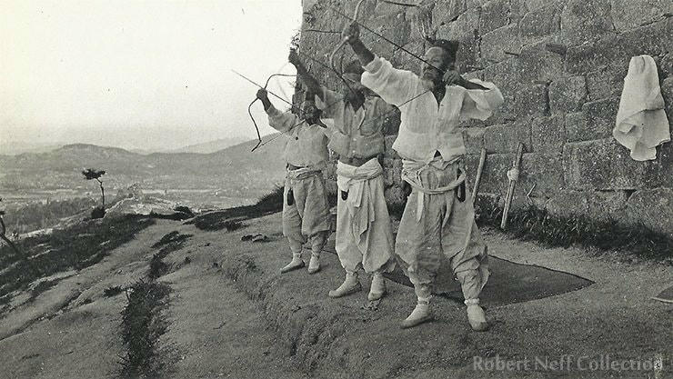 Cung thủ Hàn Quốc đứng dọc theo những gì trông giống như một phần của bức tường thành phố. Khoảng những năm 1930. Ảnh: KT.