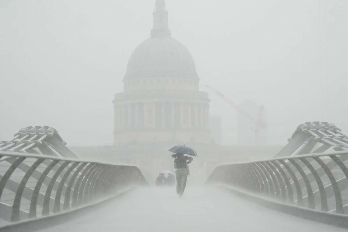 Những người cầm ô đi dưới mưa trên cây cầu Millennium. Sau nhiều tuần thời tiết oi bức, Met Office đã đưa ra cảnh báo giông bão khi mưa xối xả đổ bộ vào các vùng của Anh và xứ Wales. Ảnh: Victoria Jones / PA.