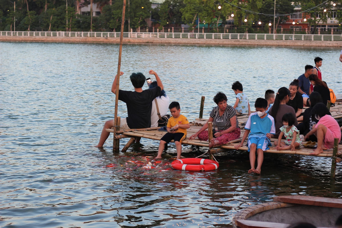 Người dân thích thú với trải nghiệm ngồi trên cầu tre ngâm nước và cho cá ăn.