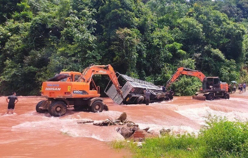 Xe tải bị lật nghiêng khi đi qua điểm bị ngập, dòng chảy mạnh. Lực lượng chức năng, người dân địa phương phải chèn bánh và dùng xe cẩu nỗ lực kéo xe tải ra khỏi vị trí nguy hiểm. (Ảnh: TTXVN phát)