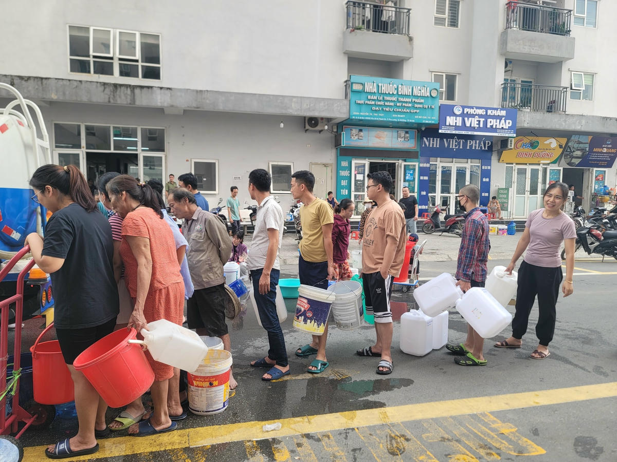 Người dân với xô chậu, thùng, can nhựa trên tay, xếp hàng tới lượt lấy nước.