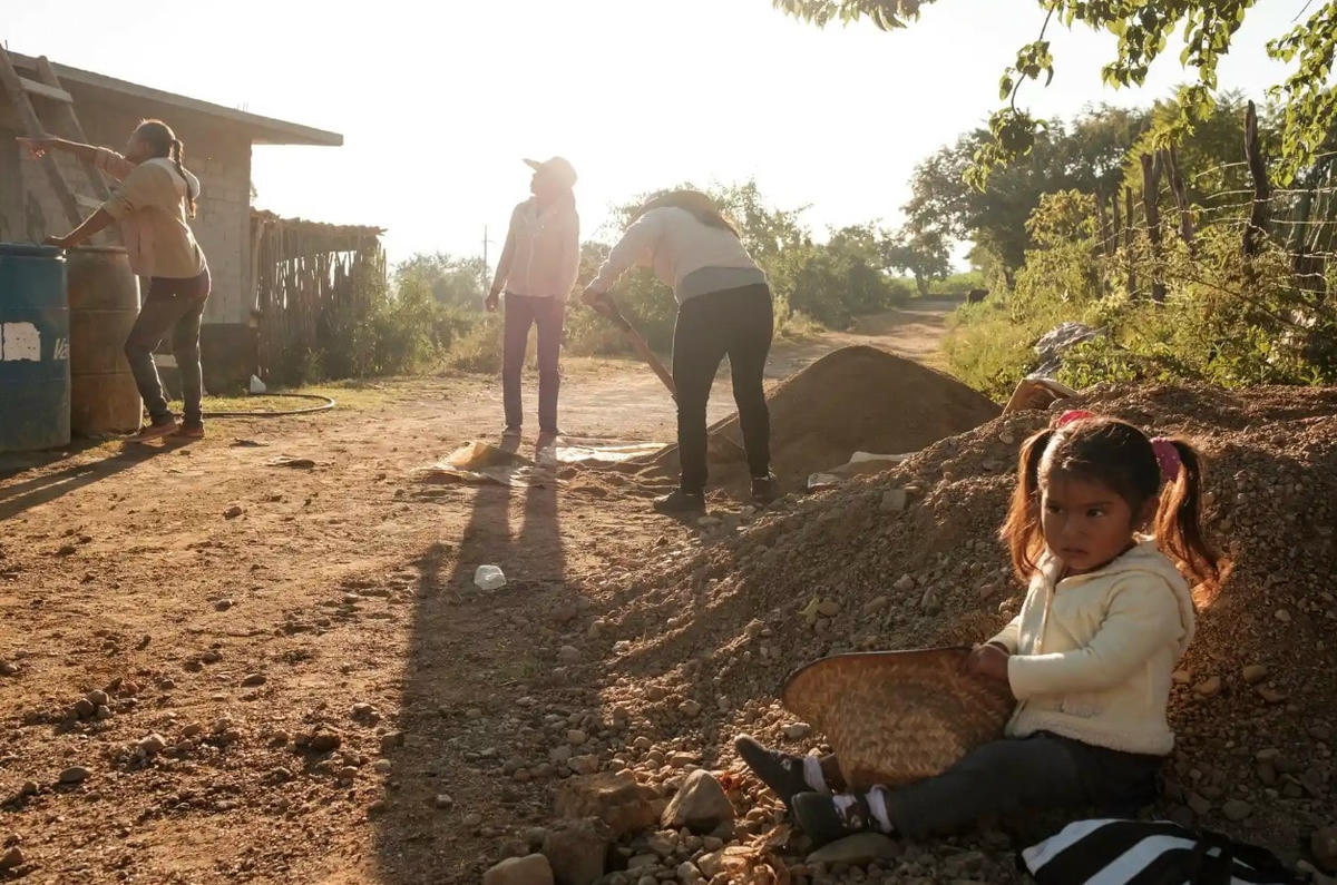 Một cô gái trẻ chơi đùa trong khi một nhóm phụ nữ xây bể thu nước mưa ở Mogote Colorado, một ngôi làng thuộc thành phố Santiago Ayuquililla, bang Oaxaca. Ảnh: The Guardian.