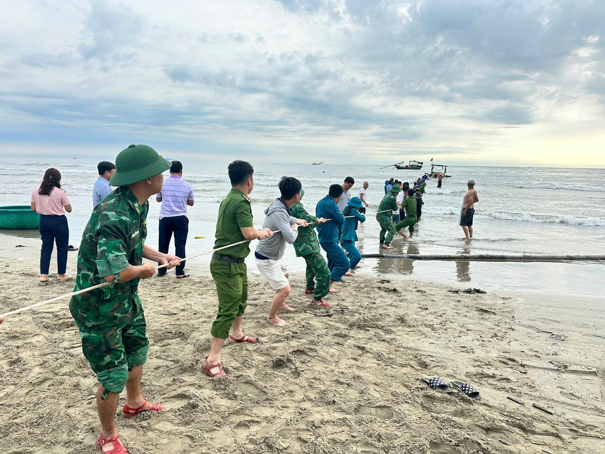 Lực lượng phối hợp nỗ lực kéo thuyền của ngư dân bị sóng đánh chìm lên bờ. Ảnh Hạnh Nguyên.