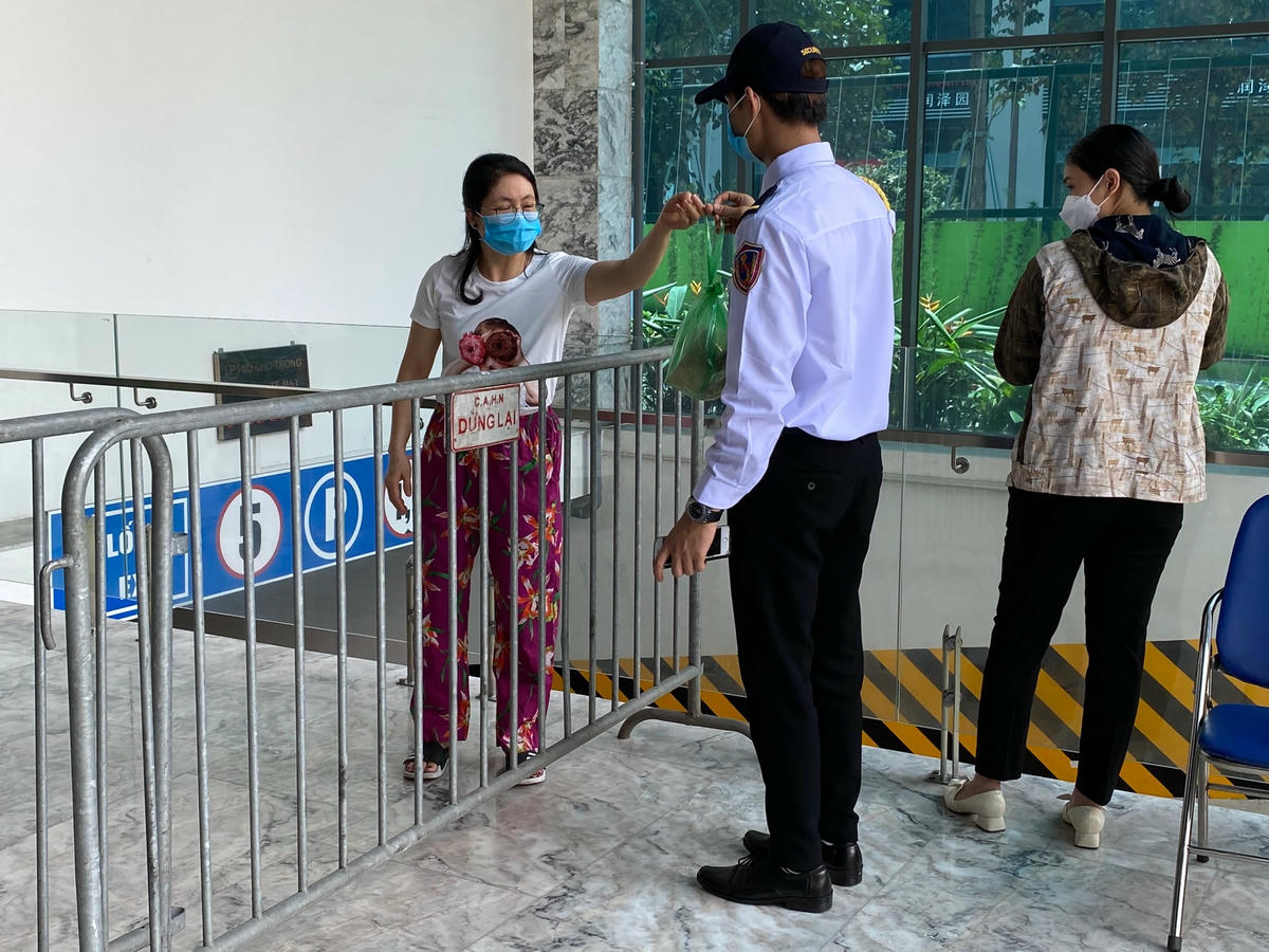 Lực lượng bảo vệ hỗ trợ người dân nhận đồ nhu yếu phẩm. Ảnh: Lan Anh.