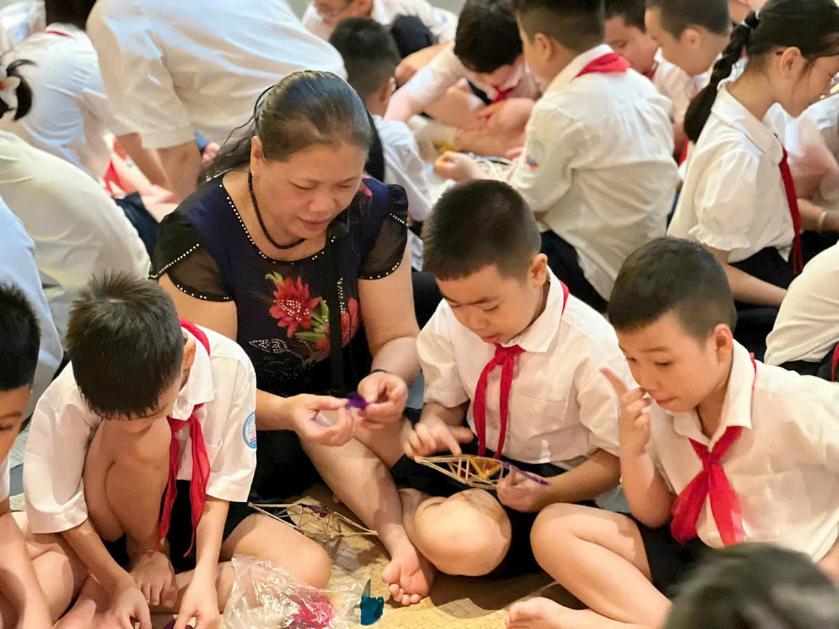 Nghệ nhân làng nghề Ái Mộ (Hà Nội) hướng dẫn các em nhỏ làm đèn ông sao. Ảnh: P. Sỹ.