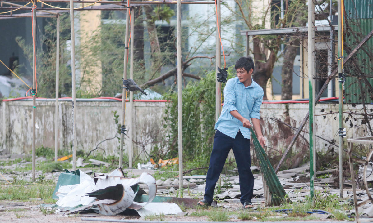 Người dân vừa phải nhặt tôn, kê lại bàn ghế, vừa theo dõi tình hình biển để đảm bảo an toàn. Ảnh: Cẩm Kỳ.