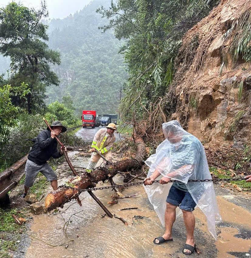 Lực lượng chức năng và người dân đang dọn dẹp đất đá, cây đổ để phương tiện có thể di chuyển được. Ảnh: Tuấn Trung.