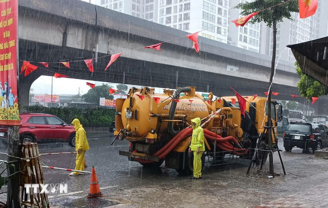 Công nhân ứng trực tiêu thoát nước trong mưa lớn tại đường Nguyễn Xiển. (Ảnh: Nguyễn Thắng/TTXVN).