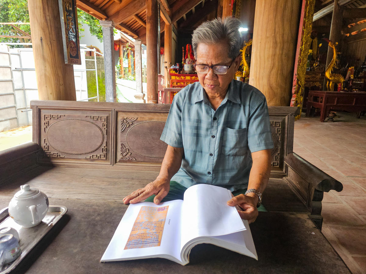 Ông Nguyễn Thế Nhịp - thủ từ đình Thanh Nga lật giở cuốn sách có hình ảnh từng sắc phong vua ban. Ảnh: Đình Minh