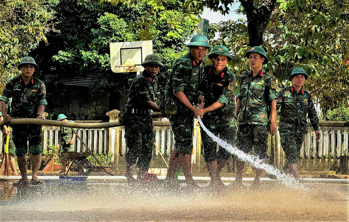 Chiến sĩ Trung đoàn Bộ binh 887 dùng vòi xịt nước rửa trôi lớp bùn đất bám trong khuôn viên trường học ở xã Bình Minh. Ảnh: CV..