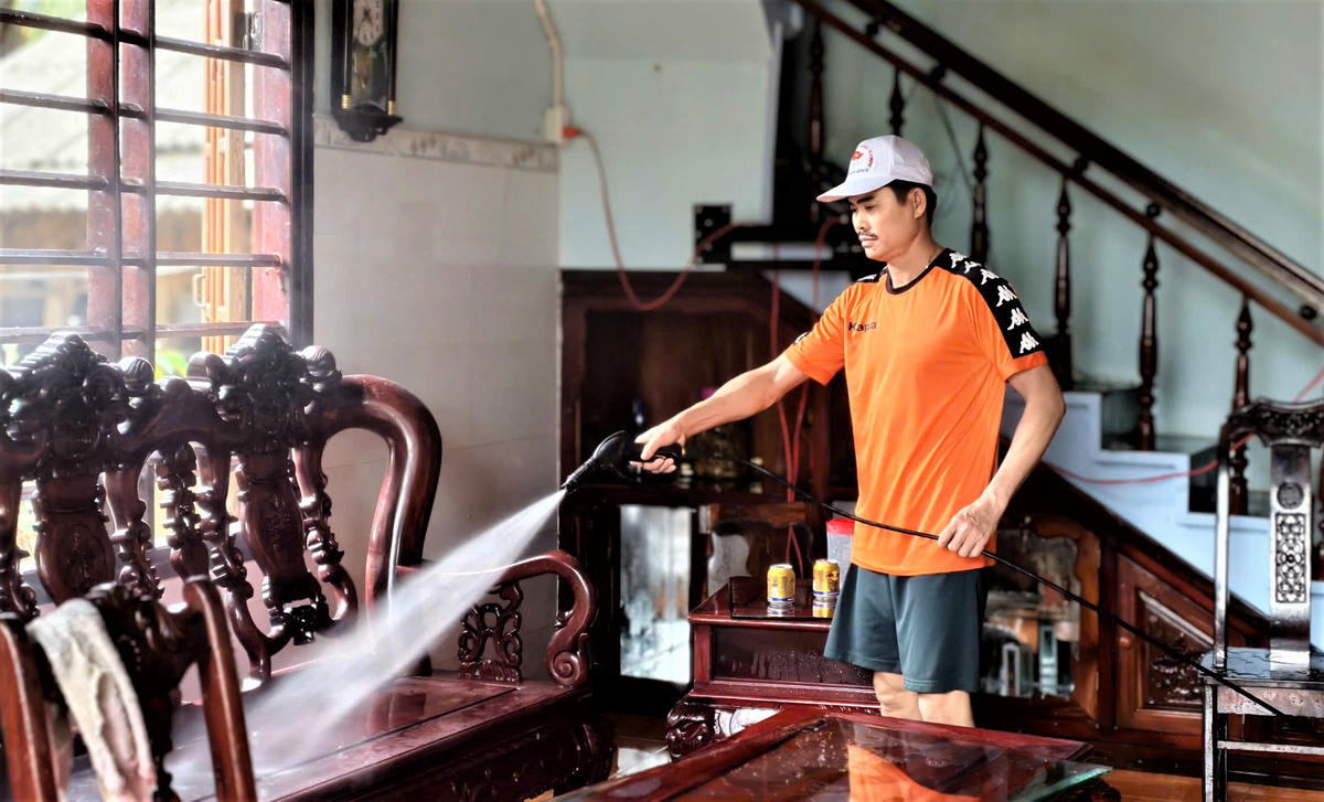 Ông Bùi Tấn Thanh dùng vòi nước xịt rửa bàn ghế. Ảnh: CV.