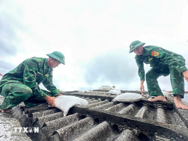 Các chiến sỹ giúp người dân đưa bao cát lên mái nhà để tránh tốc mái tôn khi gió bão. (Ảnh: TTXVN phát)