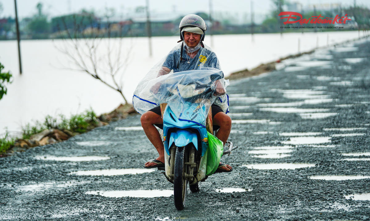 Trao đổi với Báo Đại đoàn kết, ông Hà Đức Nhanh, Phó giám đốc Công ty CP Xây dựng và Thương mại Ngọc Minh cho biết, từ đầu tháng 8/2025, đơn vị đã huy động nhân lực, máy móc, vật liệu, dựng lán trại để triển khai công việc. nhiều vị trí nền cũ bằng bê tông xi măng đã được đục bỏ và dặm vá bằng lớp base, những điểm hư hỏng nặng đang được khắc phục trước khi thảm hai lớp bê tông nhựa hoàn thiện. Dự kiến sau khi hoàn thành, mặt đường sẽ cao hơn nền cũ từ 40 – 60 cm, góp phần tránh ngập úng cục bộ khi mưa lớn. Ảnh: Cẩm Kỳ 