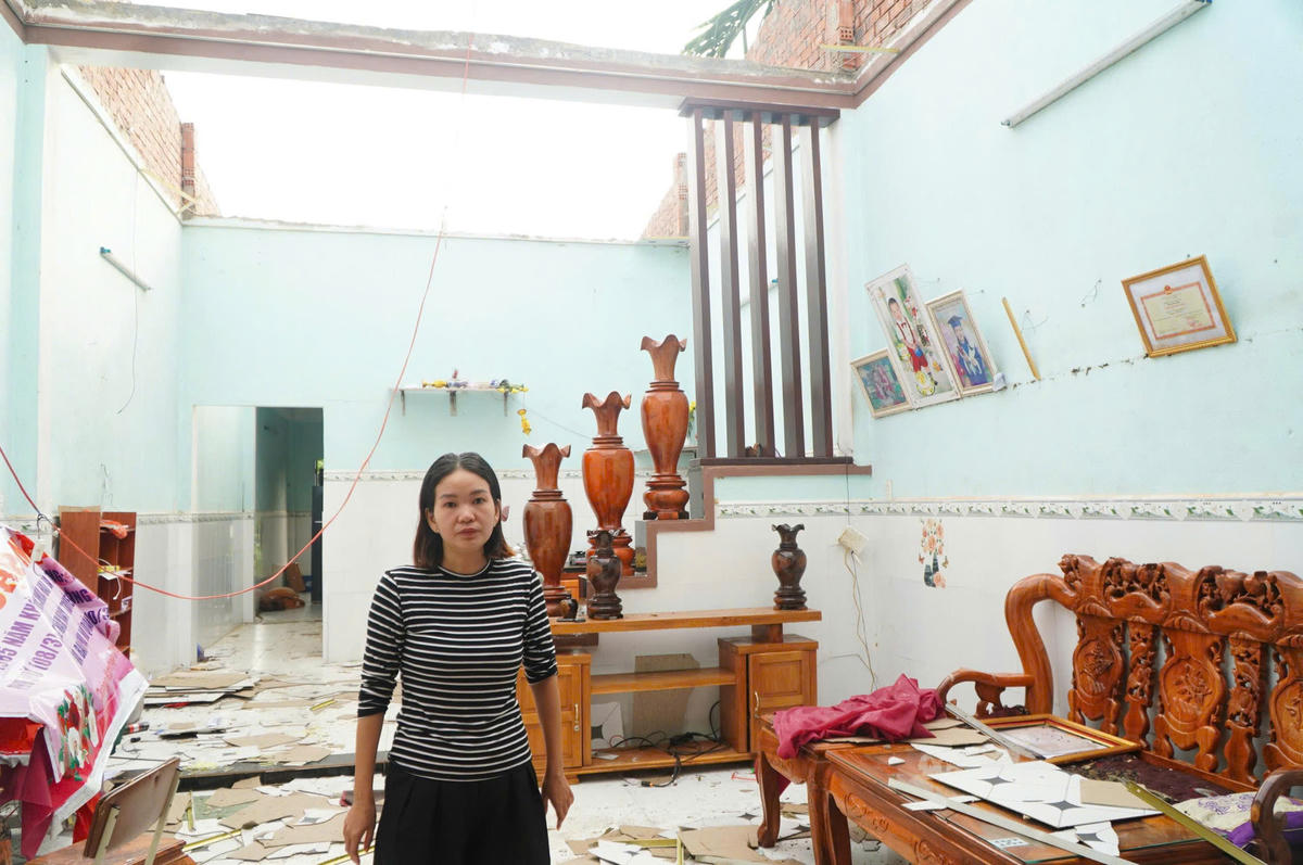 Chị Lê Thị Mỹ Nga đứng trước ngôi nhà bị lốc xoáy làm tốc mái nhà. Ảnh: Tấn Thành.
