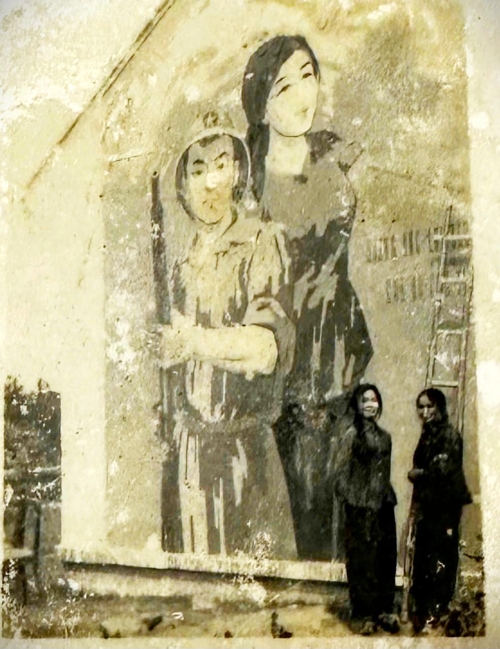 Bà Đặng Thị Ty (bên trái) cùng đồng nghiệp đứng dưới bức tranh cổ động do bà tự tay vẽ. Ảnh: nhân vật cung cấp.