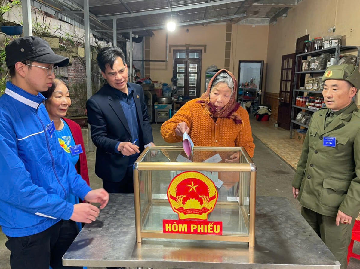 Cán bổ mang hòm phiếu phụ đến tận nhà cử tri cao tuổi, sức khỏe yếu, không thể trực tiếp đến khu vực bỏ phiếu để cử tri được thực hiện quyền bầu cử của mình. Ảnh: Phường Sa Pa.