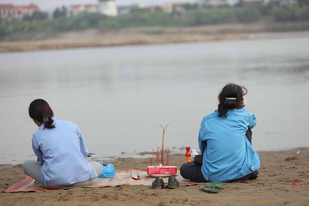 Người nhà nạn nhân ngồi ven sông mong ngóng tin tức của con em mình. Ảnh Phạm Chiểu.