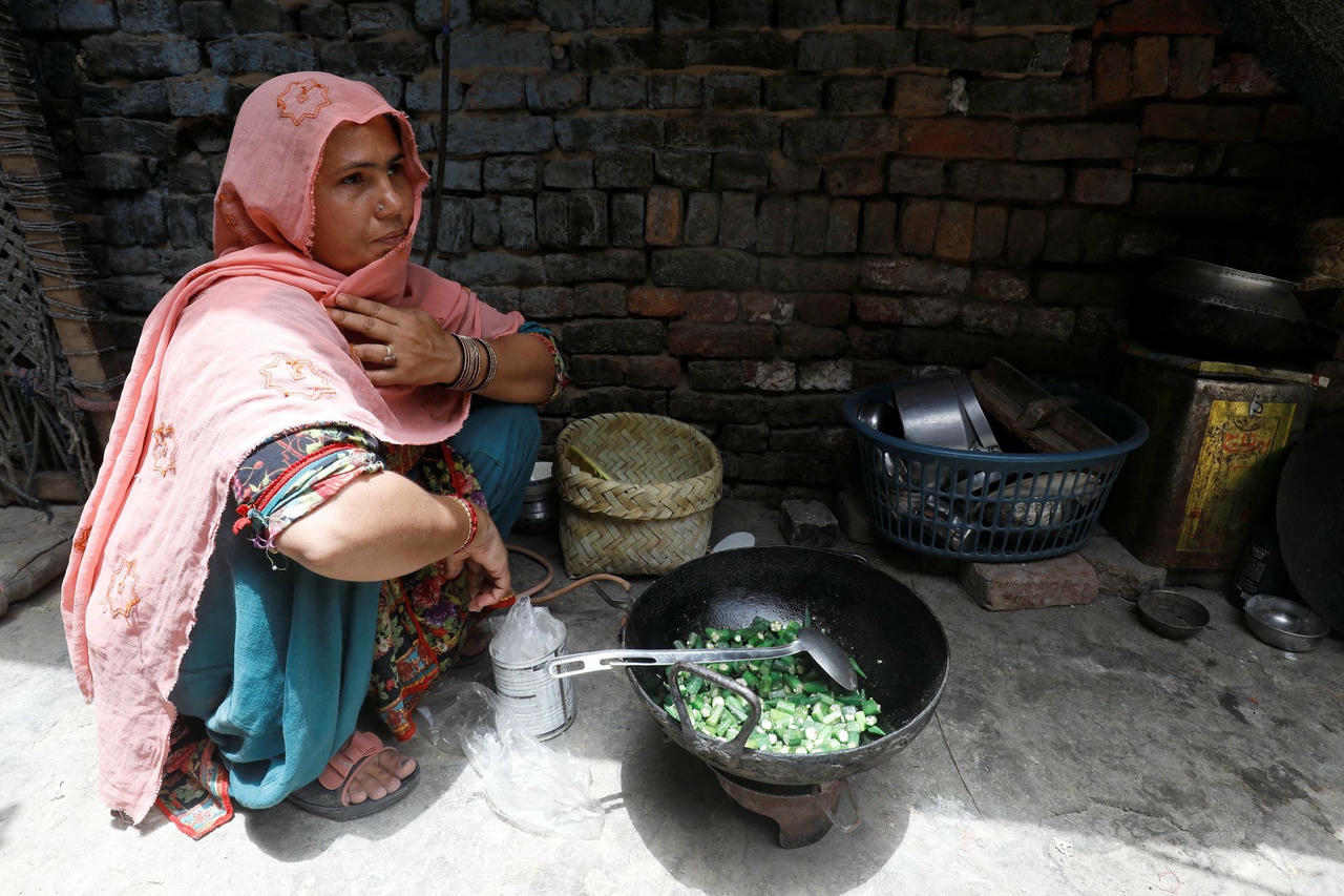Rubina, hàng xóm của Razia, rán hành tây và đậu bắp trên ngọn lửa trần. Ảnh: Reuters.