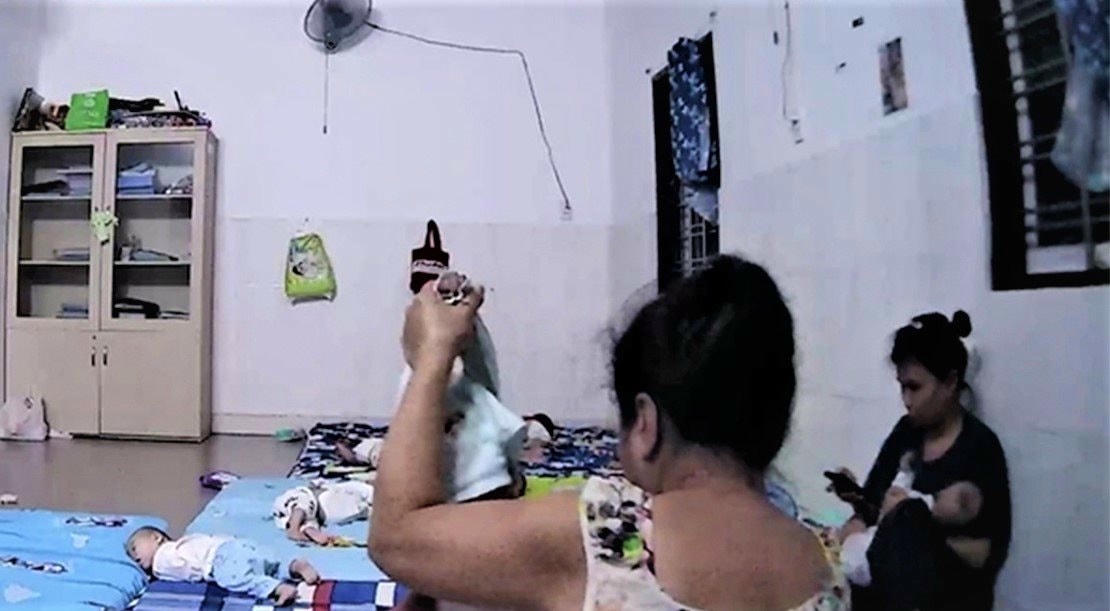 Hình ảnh một em bé khoảng 1 tháng tuổi bị bảo mẫu xách tay nhấc bổng trong lúc thay khăn tại Mái ấm Hoa Hồng.