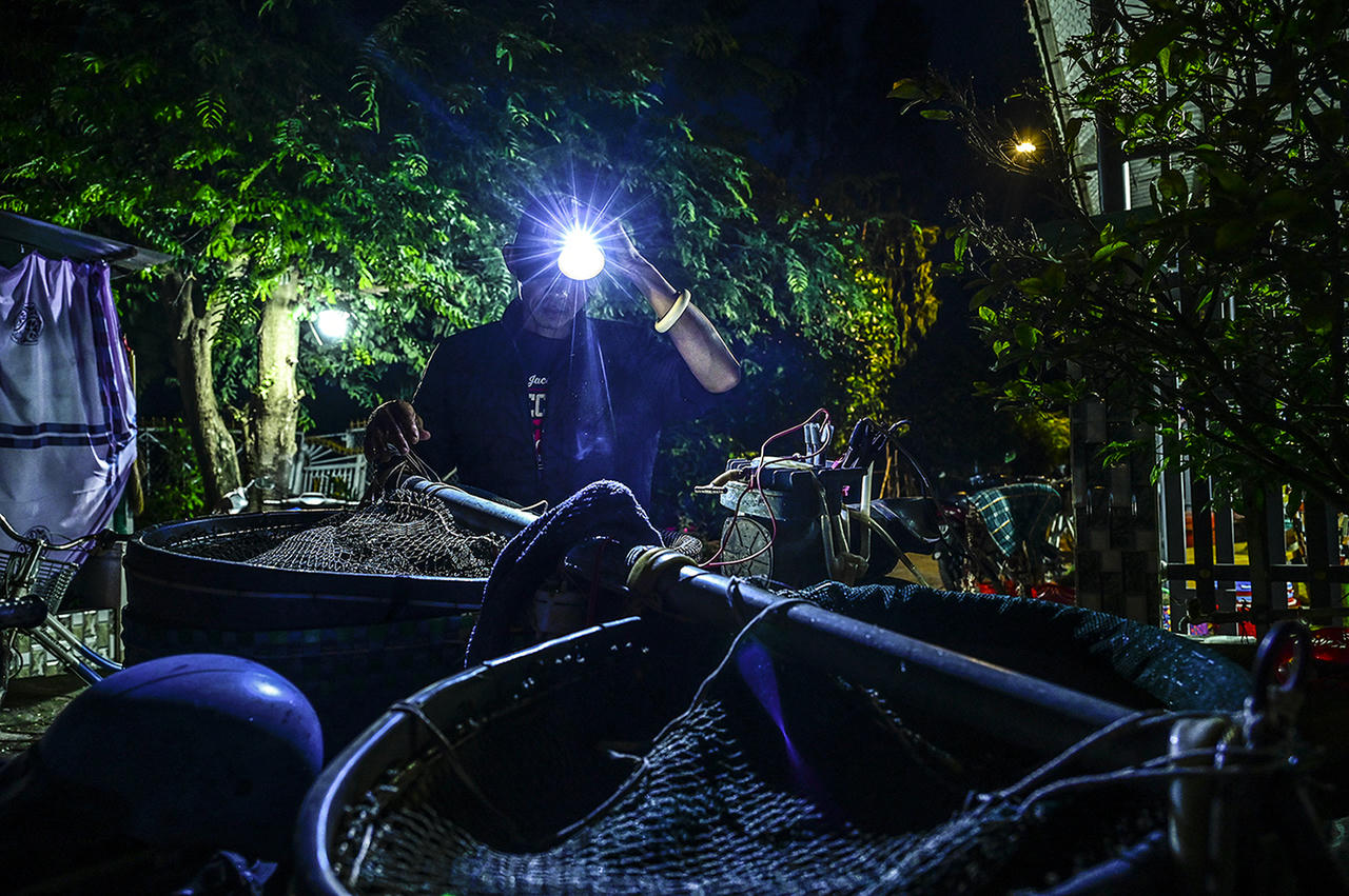 Một người dân rọi đèn pin đem cá ra chợ bán. Ảnh Nguyễn Minh
