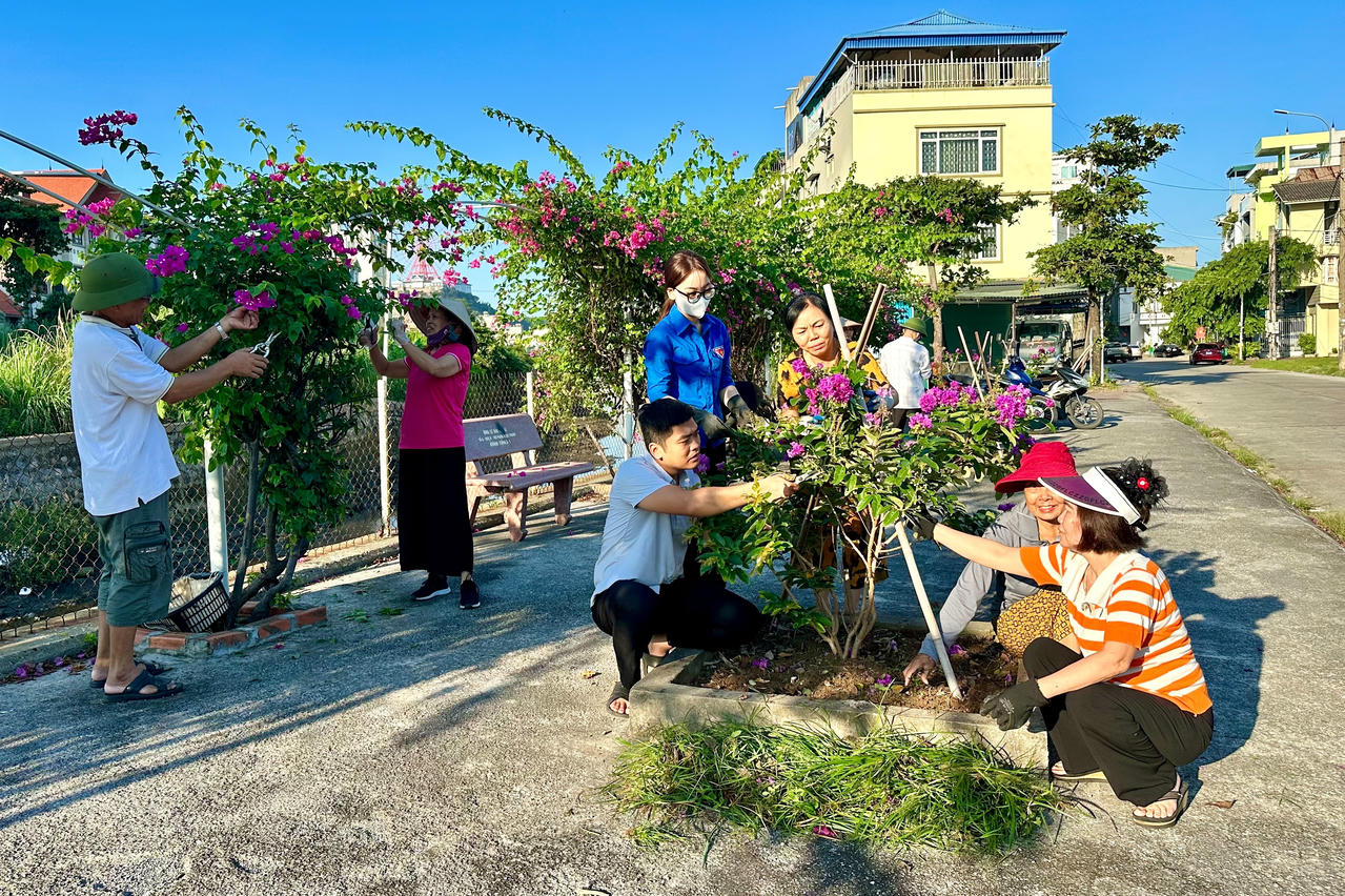 Anh Nguyễn Linh, Trưởng Ban CTMT khu phố 8 (phường Cao Xanh) cùng bà con trong khu phố trò chuyện và chăm sóc tuyến đường hoa Phạm Ngọc Thạch. Ảnh: Ngọc Anh