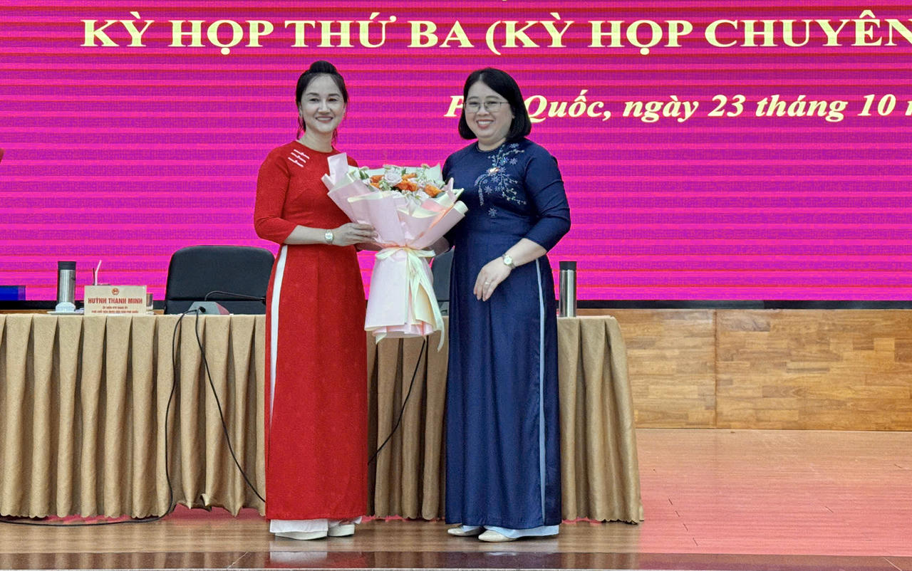 Phó bí thư Thường trực Đảng uỷ đặc khu, Chủ tịch HĐND đặc khu Phú Quốc Đặng Thị Hồng Gấm tặng hoa chúc mừng bà Nguyễn Thị Kim Loan (áo dài đỏ). Ảnh: XUÂN MI