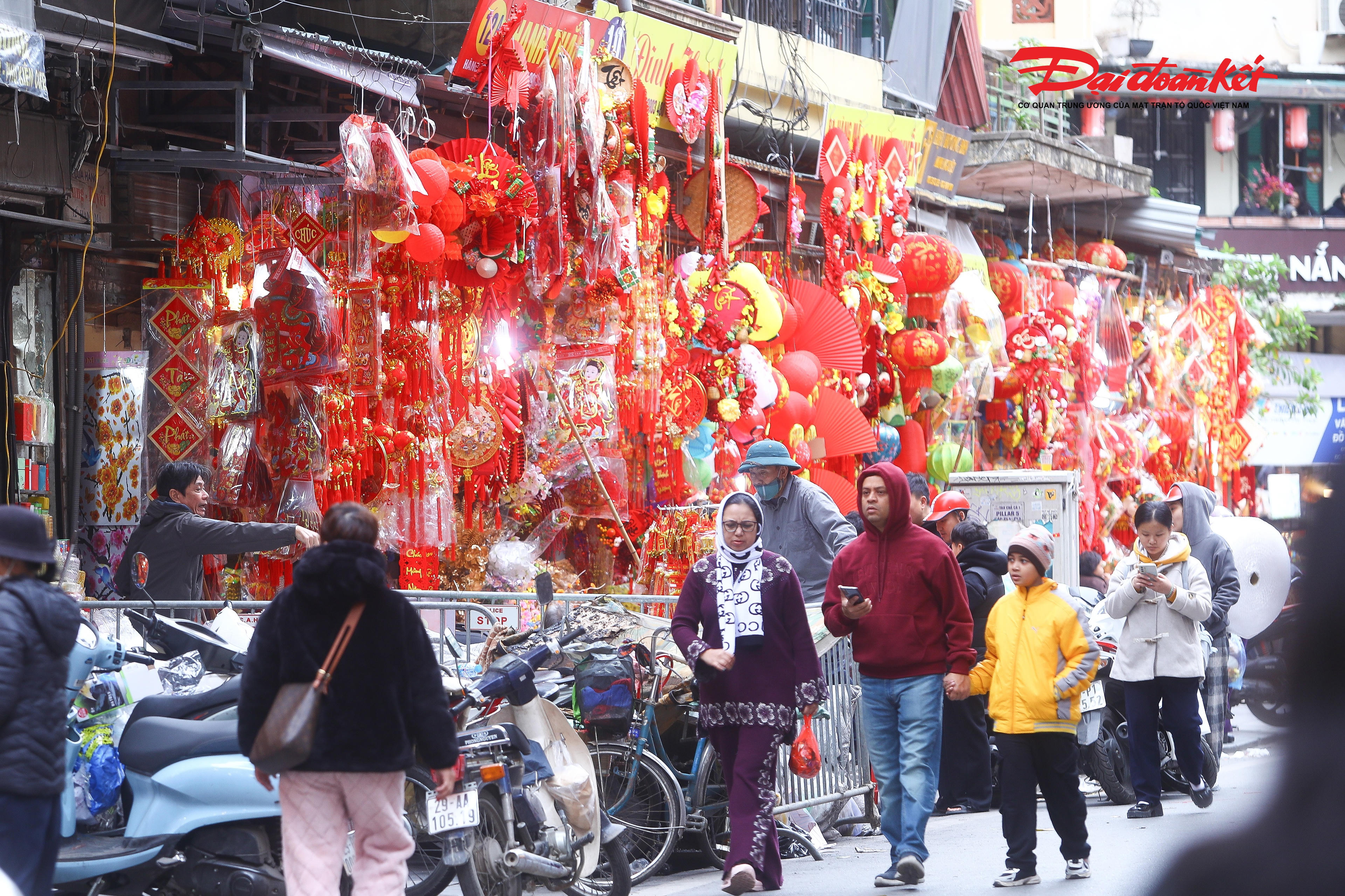 Theo ghi nhận của PV Báo Đại đoàn kết, từ sáng sớm 6/1 các cửa hàng trên phố Hàng Mã đã đồng loạt mở cửa, hàng hóa được bày kín từ trong nhà ra ngoài vỉa hè. Những chùm đèn lồng đỏ treo cao, giấy trang kim lấp lánh dưới nắng đông, câu đối đỏ in chữ vàng nổi bật. Không gian nơi đây như một bức tranh nhiều lớp màu sắc, vừa sôi động vừa ấm áp, khiến bất cứ ai đi ngang cũng khó lòng bước qua mà không ngoái nhìn.